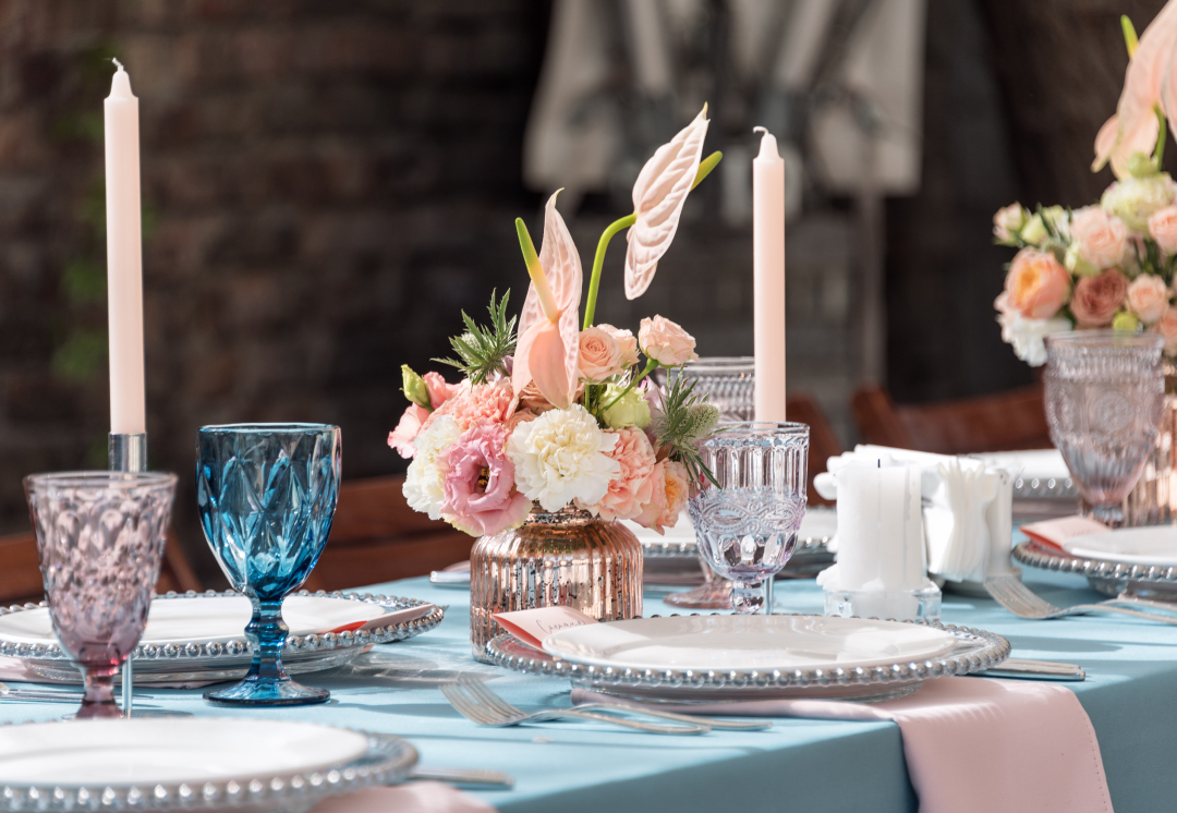 Festlich gedeckter Tisch mit Kerzen, bunten Weingläsern, Blumen und Tischdecke